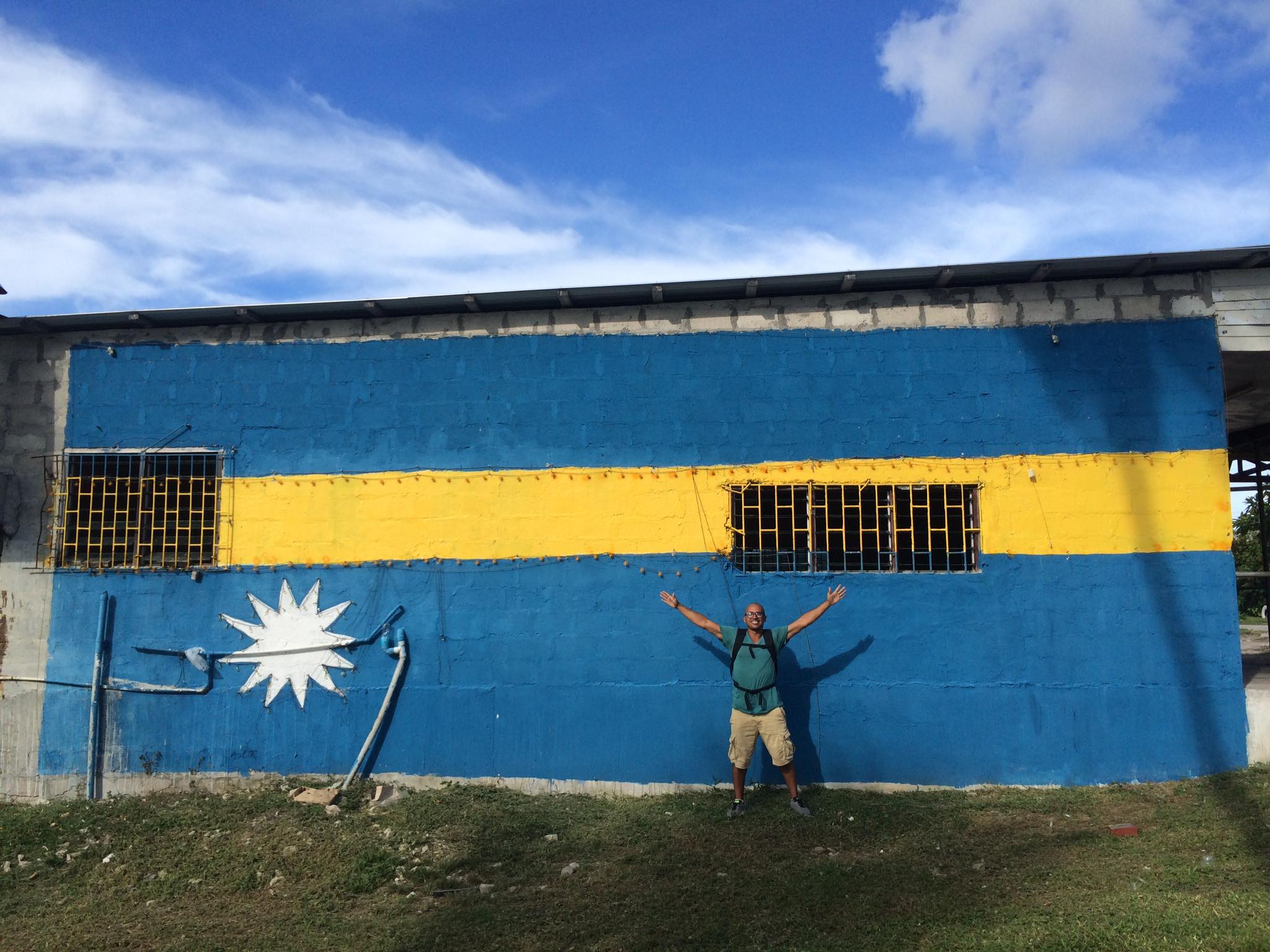 A proud moment captured as the I stand in front of a vibrant mural featuring the flag of Nauru on Nauru Island. The mural, depicting the Nauruan flag with its distinctive blue background and a white star in the center, stands as a symbol of national pride. The image reflects the my respect for the island nation's heritage and identity.