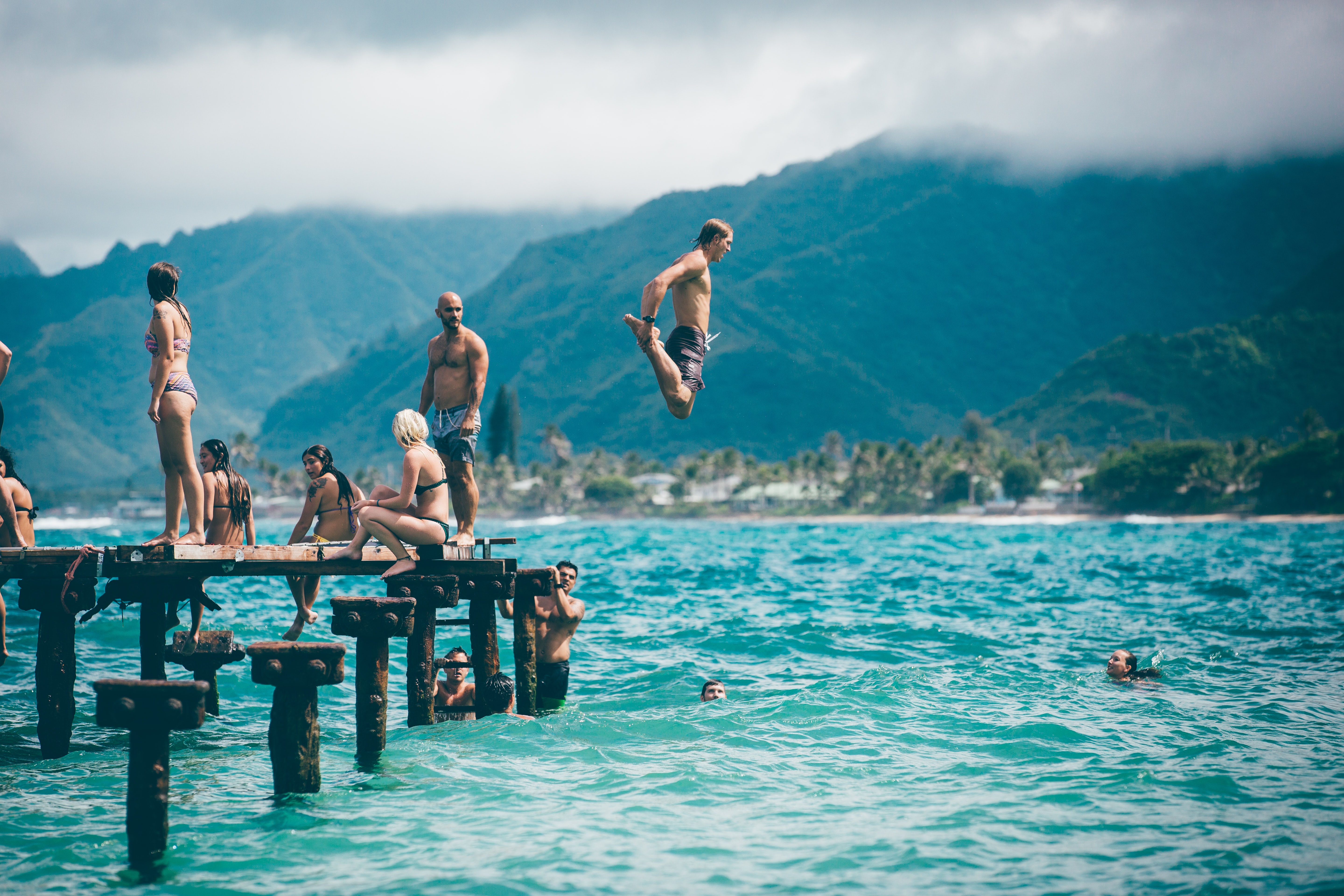friends in Hawaii swimming and jumping from a pier