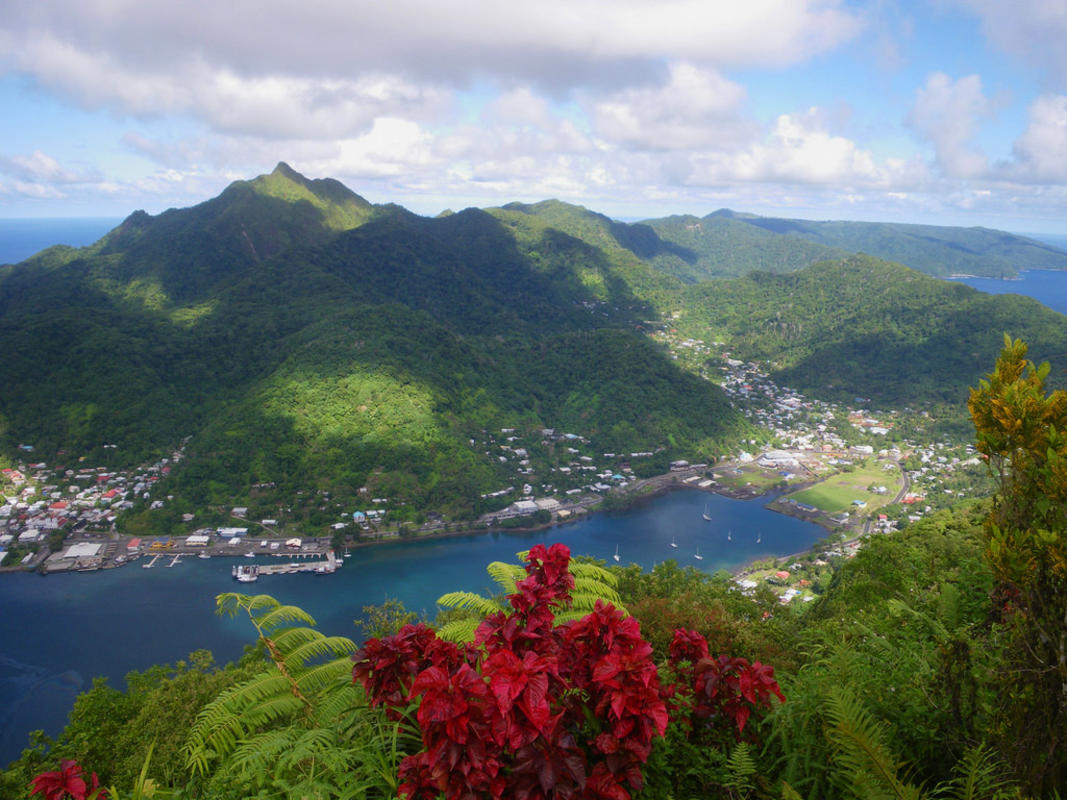 Panoramic View of American Samoa: A breathtaking landscape featuring lush green mountains cascading down to meet the turquoise waters of the Pacific Ocean.