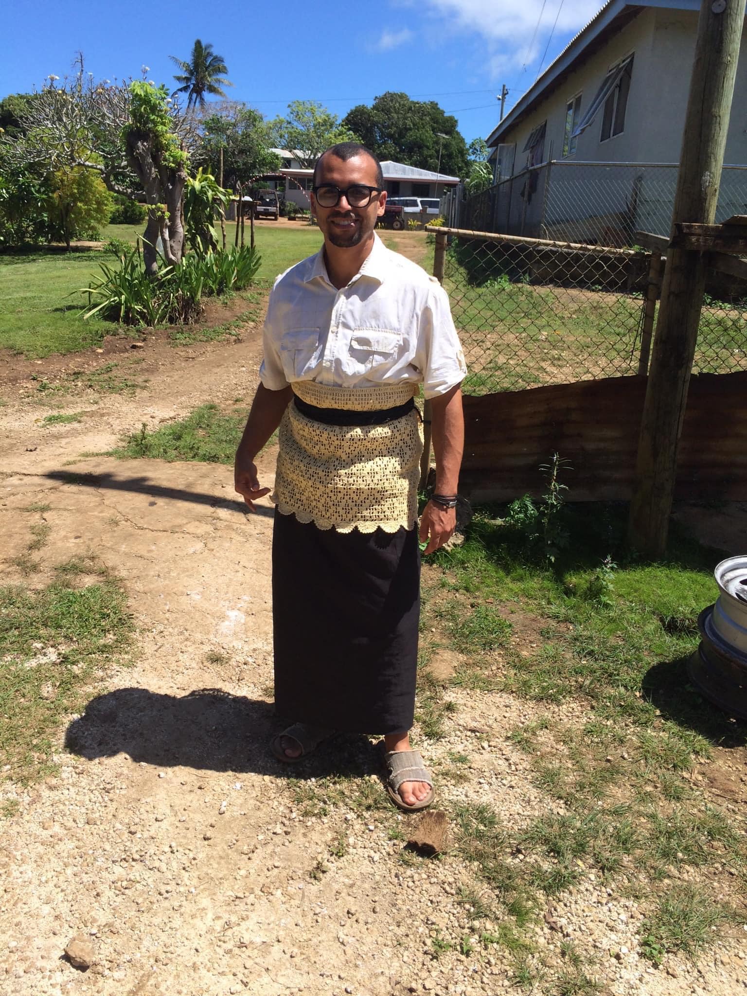 A person wearing traditional Tongan attire, consisting of a tupenu (a woven skirt) and a ta'ovala (a waist mat made from woven pandanus leaves). The person is standing in a picturesque setting in Vava'u, Tonga, representing the rich cultural heritage of the Pacific Islands