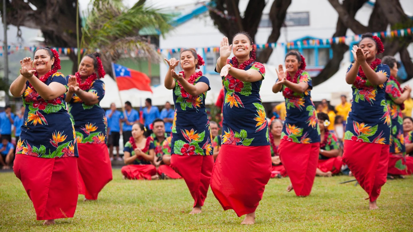 women of samoa dancing in a field with samoan flag in backgroud